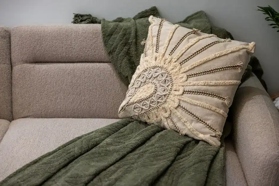 A beige sofa layered with a textured pillow and a green throw