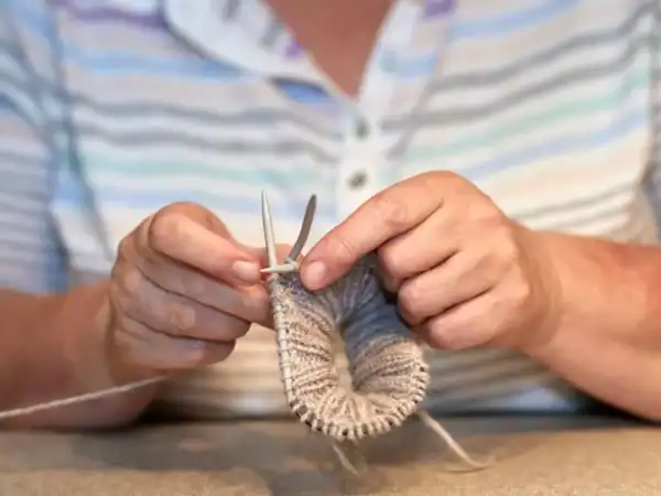 An older person's hands knitting with wooden needles