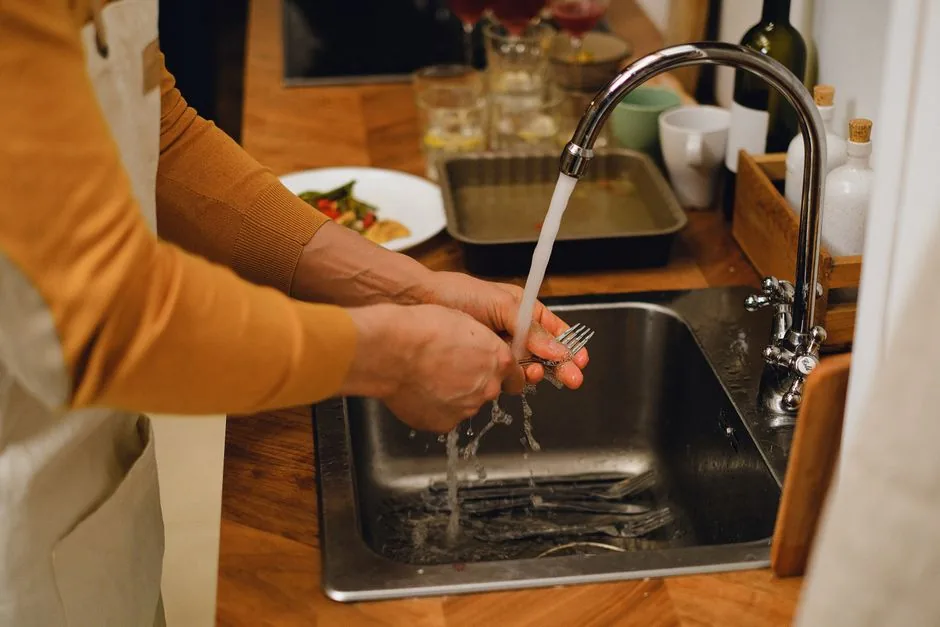 Washing cutlery under running water at the kitchen sink