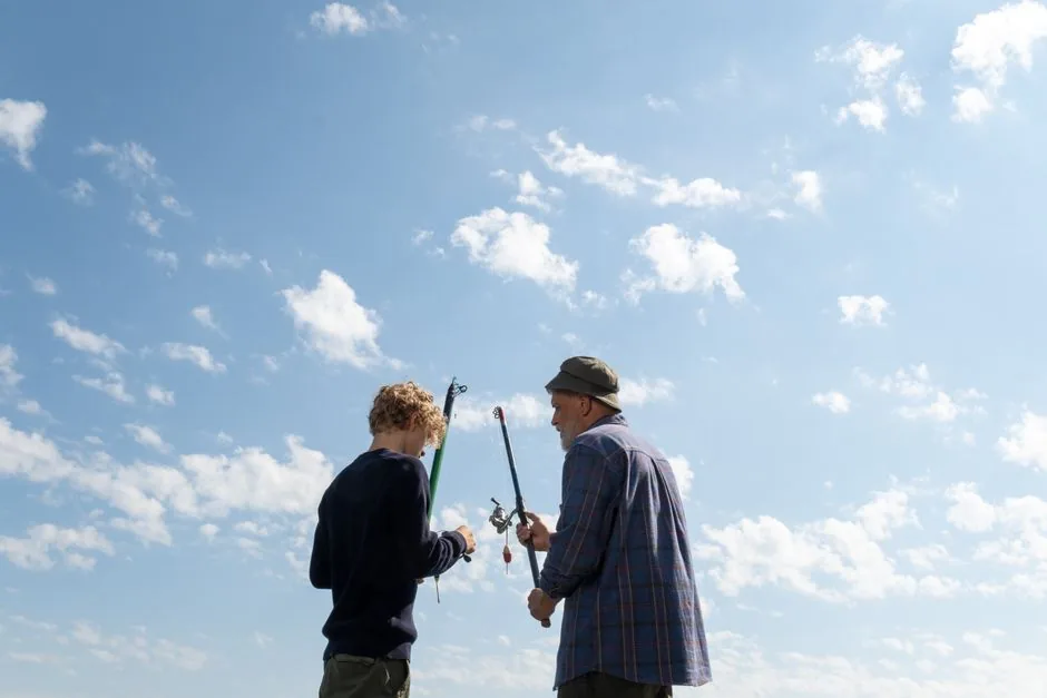 A grandfather and a boy with fishing rods under a big sky