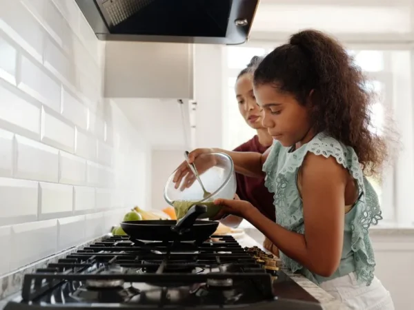 A mother teaching her daughter to cook at the stove