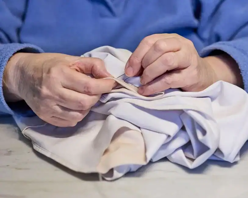Older hands mending a hem with a needle and thread