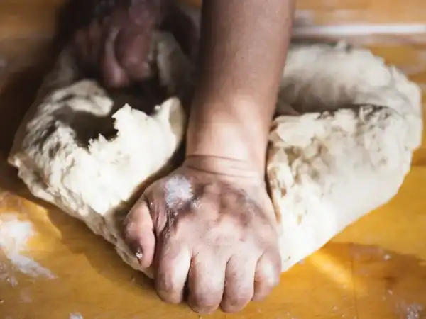 Hands kneading bread dough on a floured wooden table
