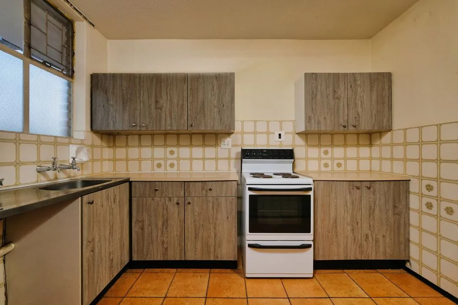 A dated kitchen with bare counters and wood cabinets