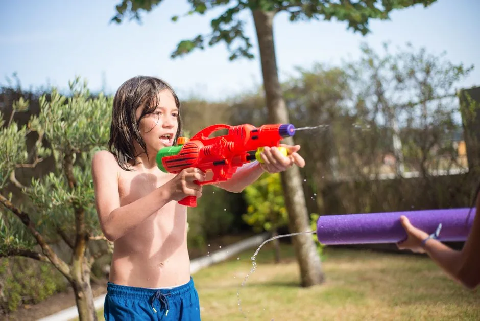 A boy soaking someone with a water toy in the backyard