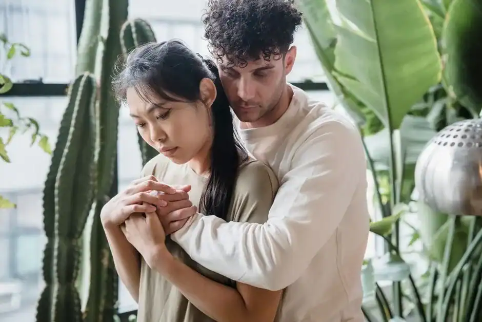 A couple shares an intimate back hug surrounded by large indoor plants.