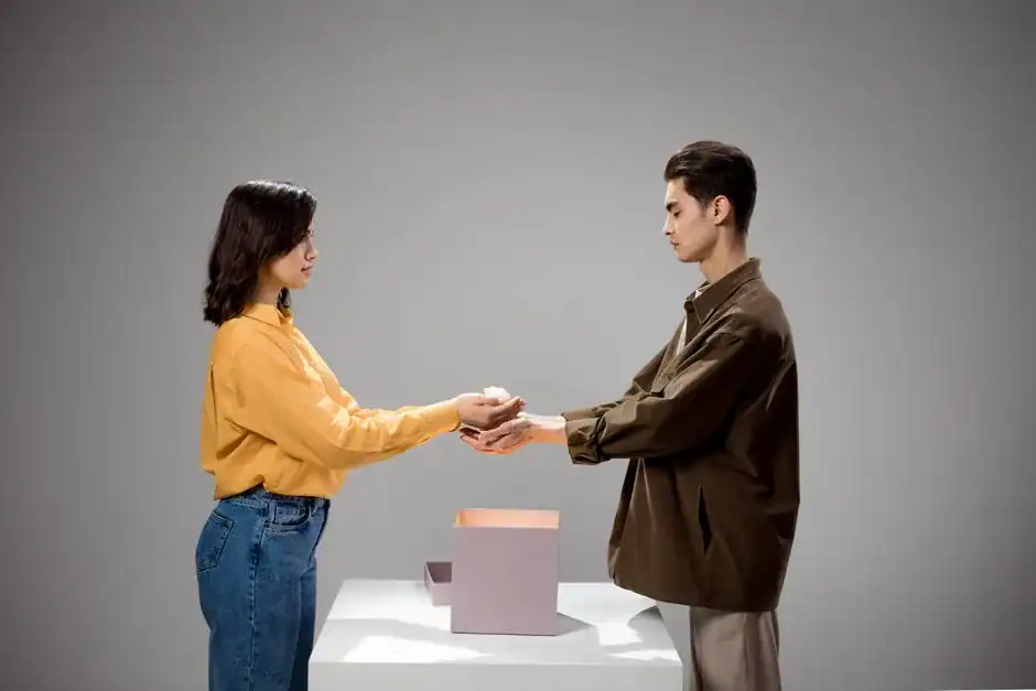 A man and woman exchanging a gift box in a studio setting with a neutral gray background.
