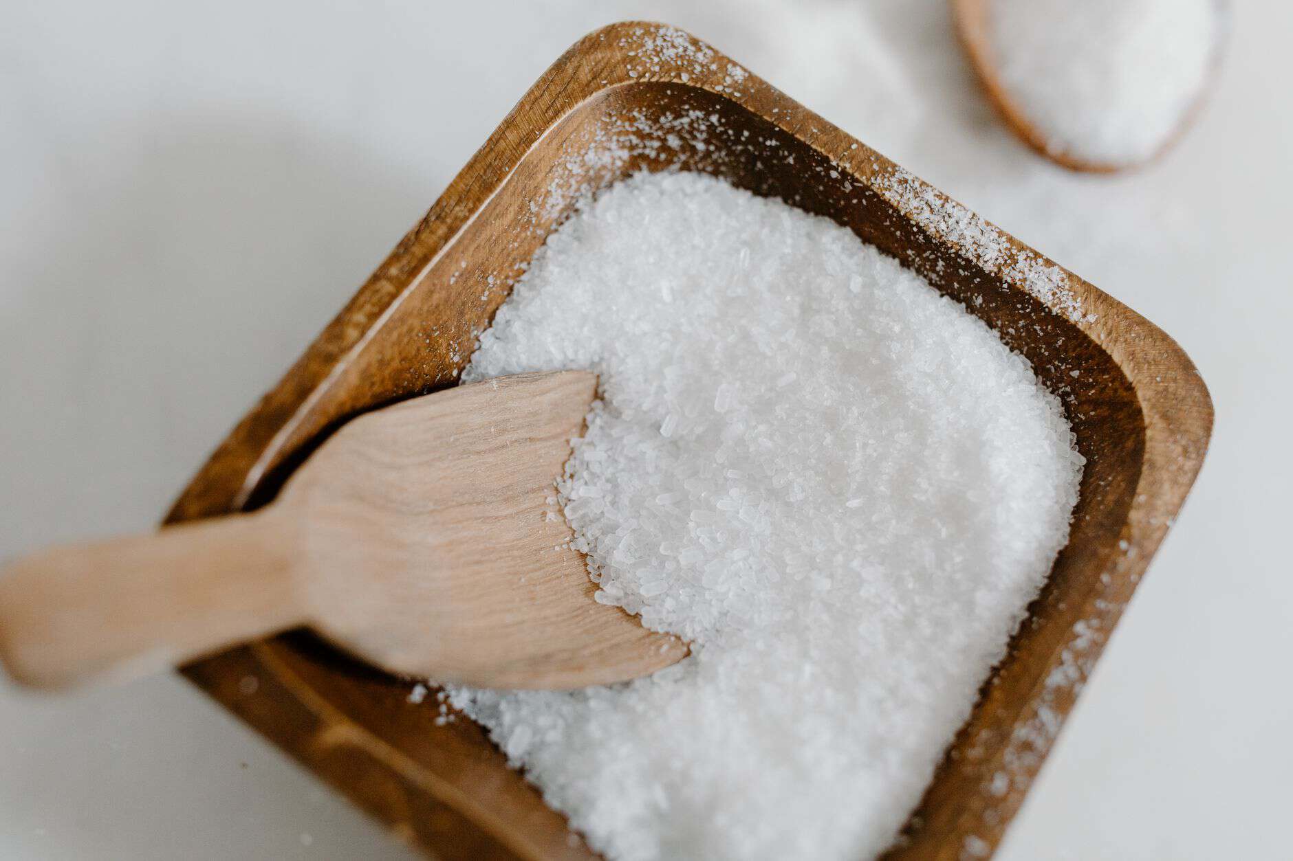 Coarse white salt in a wooden bowl with a small wooden scoop