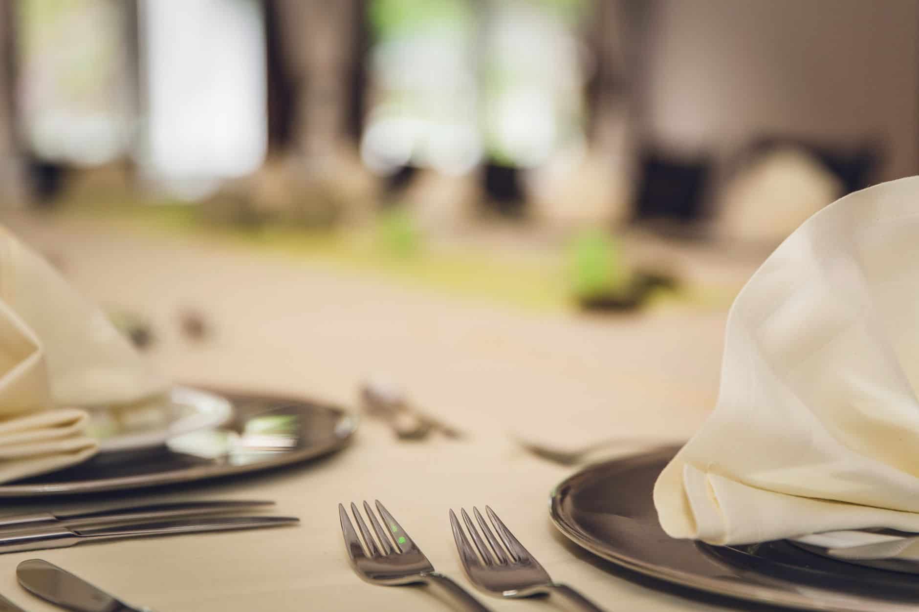 Cream cloth napkins folded on dark dinner plates with silver forks beside them