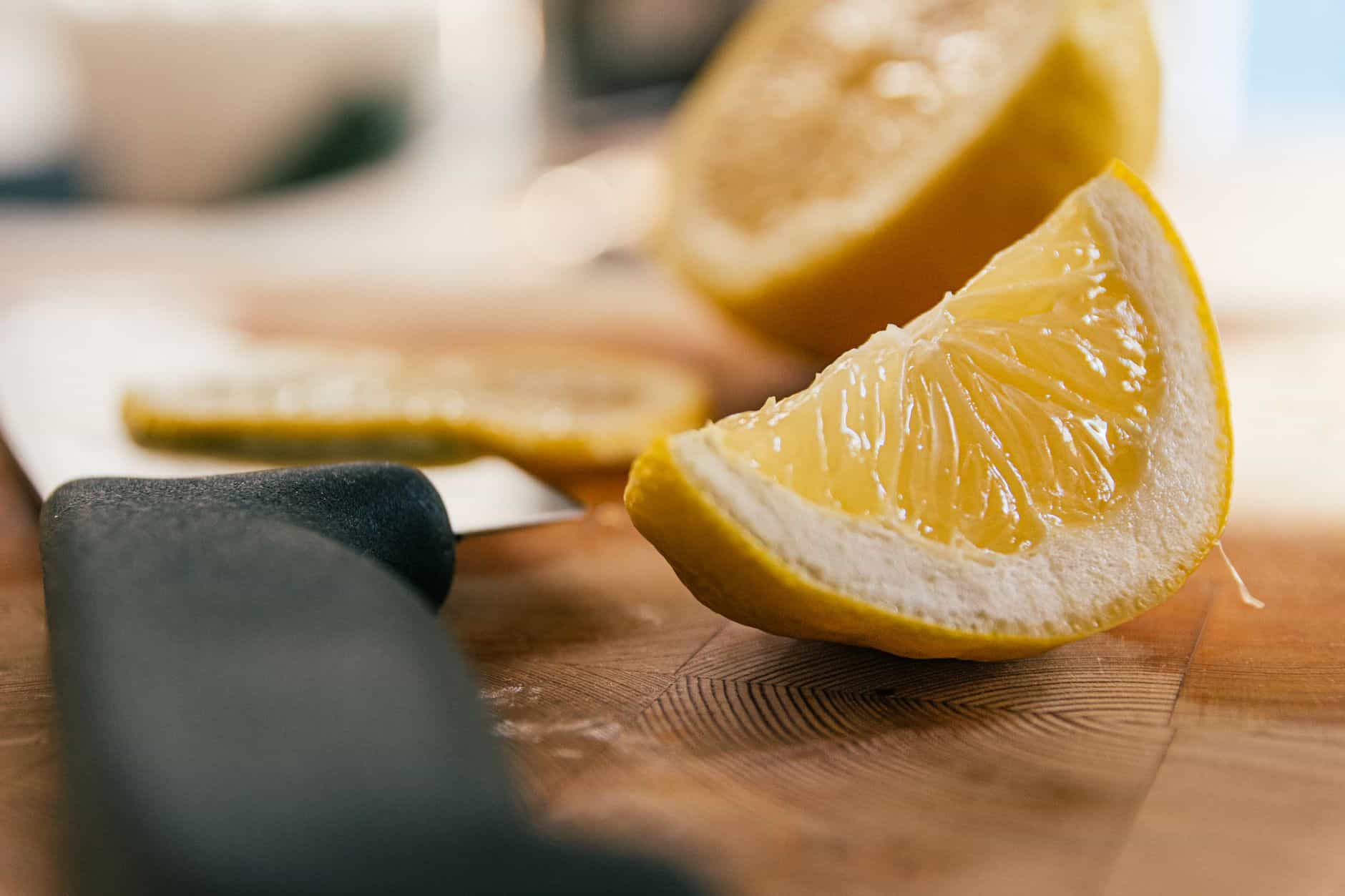Fresh cut lemon wedges on a wooden cutting board beside a knife