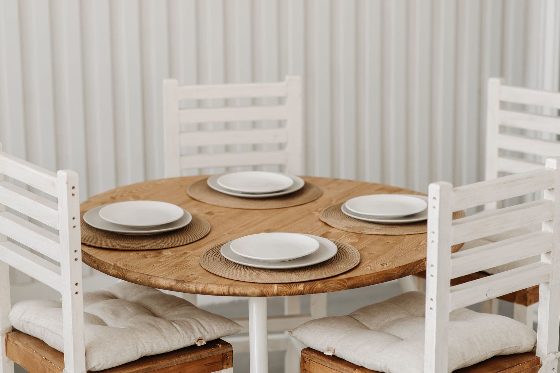 Four white dining chairs pushed in around a round wooden table set with plates