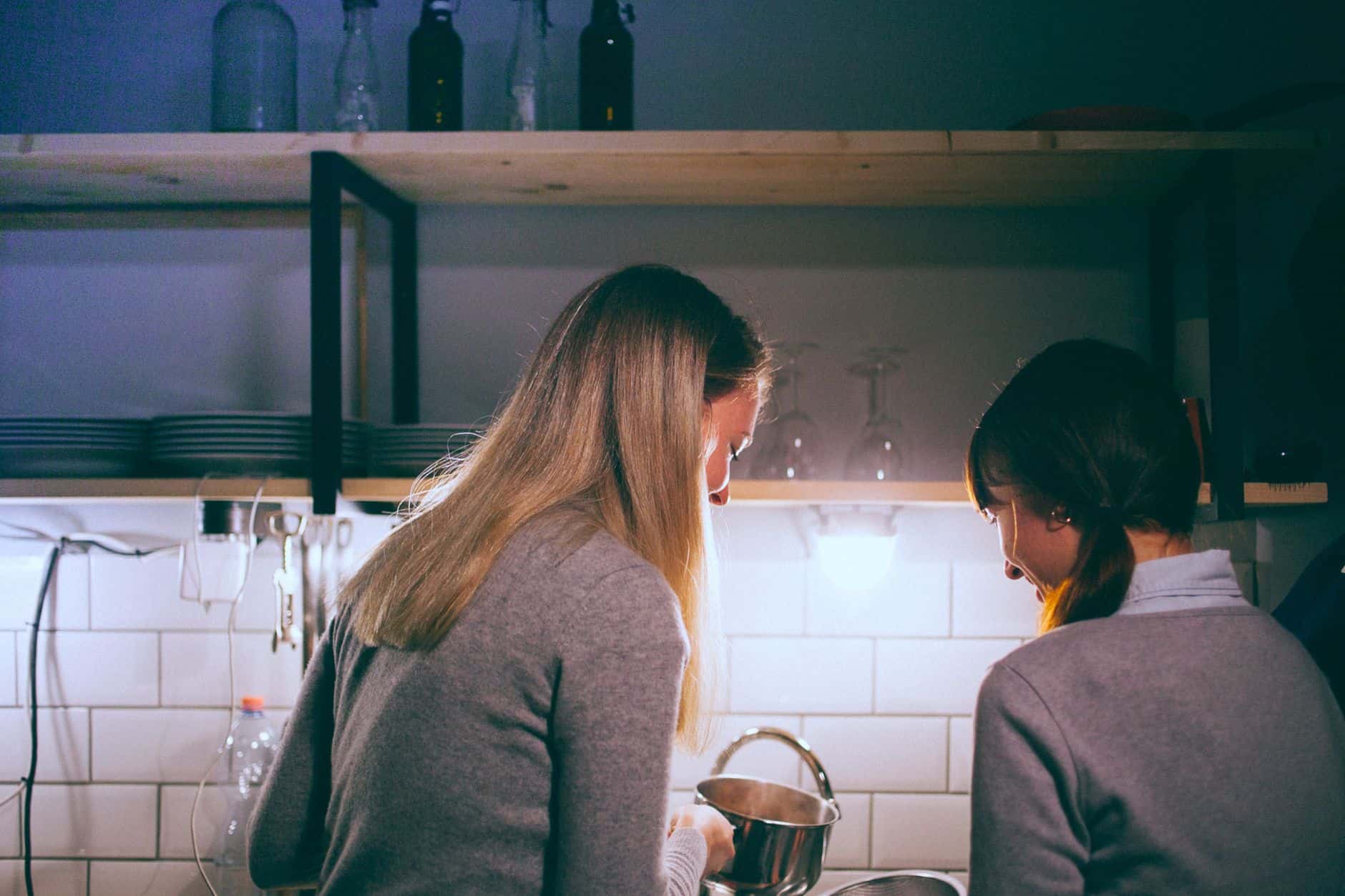 Two people standing at a kitchen sink washing a pot together after a meal