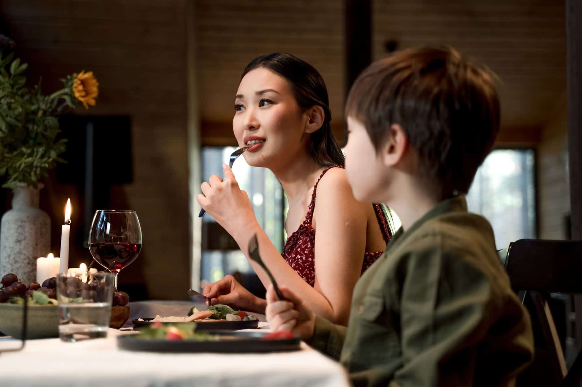 Mother eating from a fork at a candlelit dinner table while her son sits beside her with his own fork