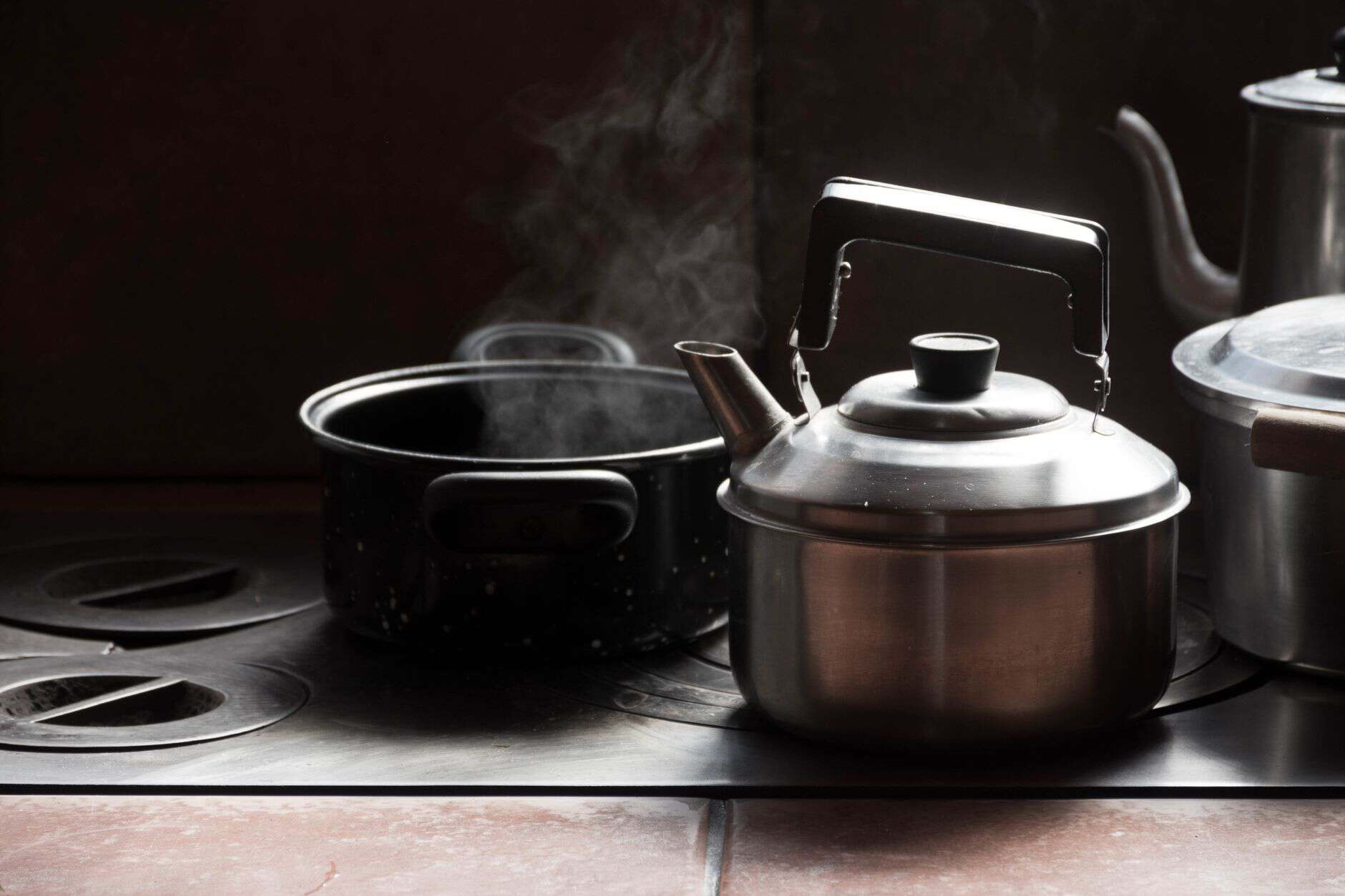 Stainless steel kettle and steaming pot sitting on an old kitchen stove