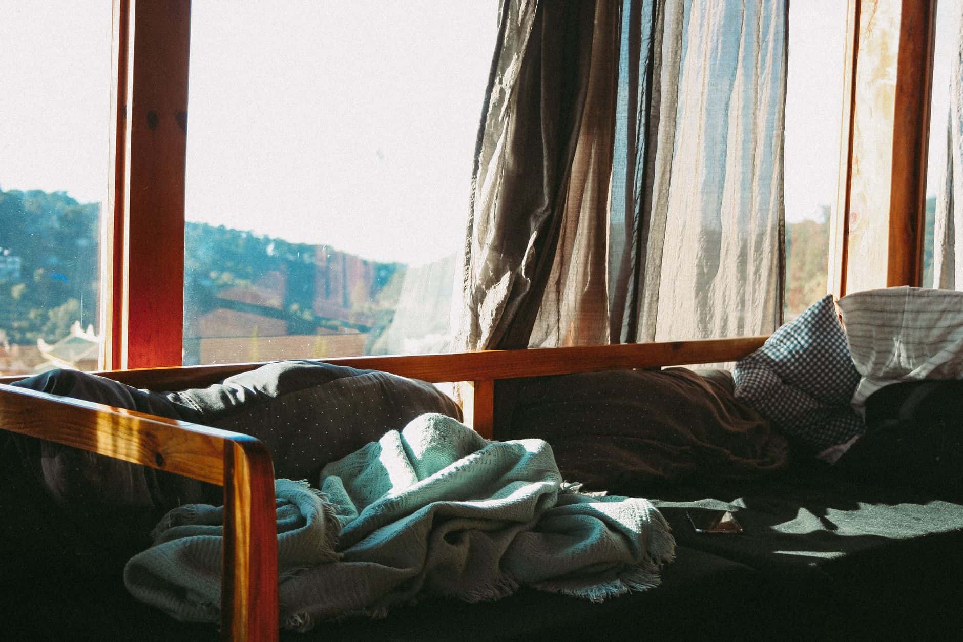 Sunlight streaming through open curtains onto pillows and a blanket by a window
