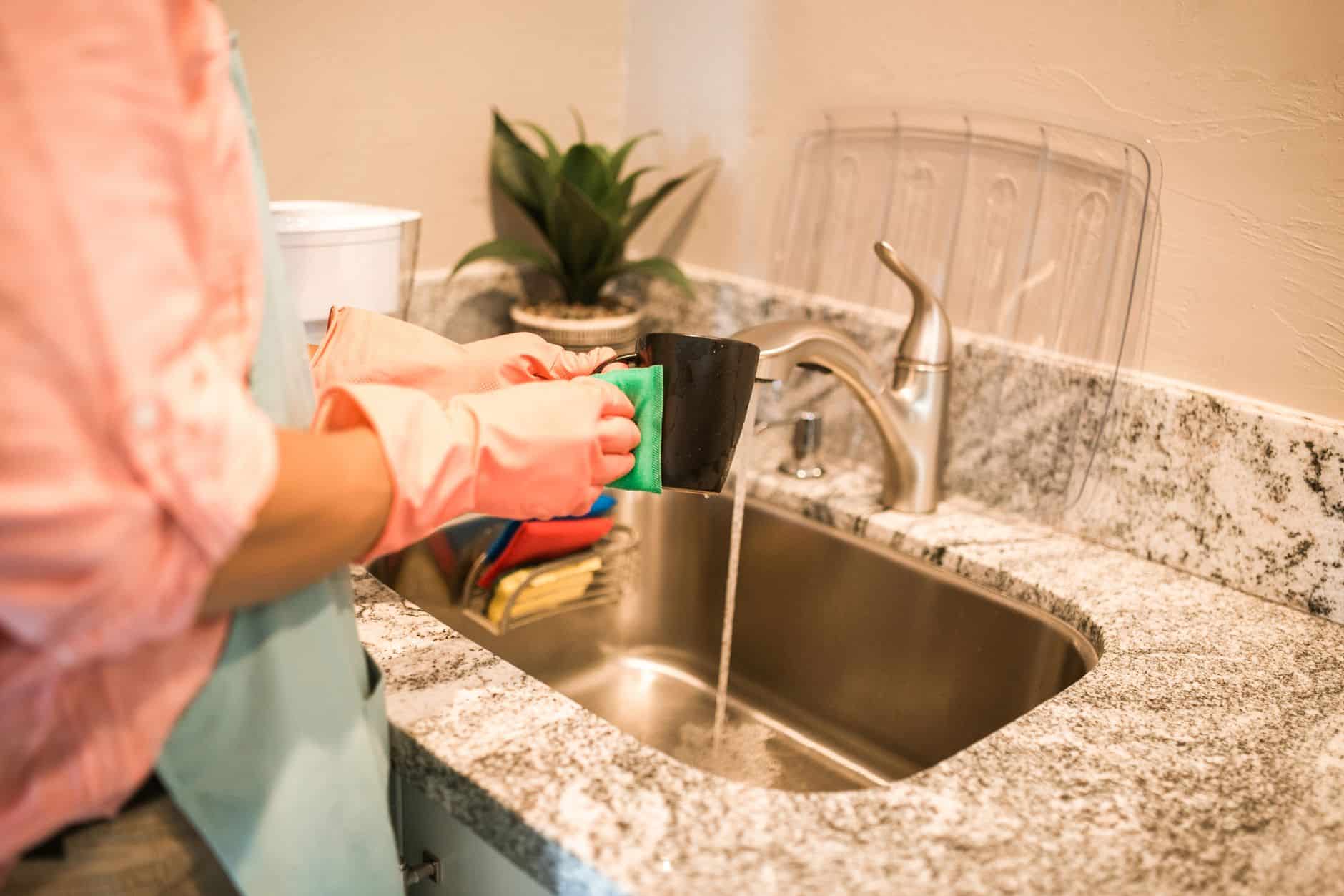 Person in rubber gloves washing a mug at a stainless steel kitchen sink