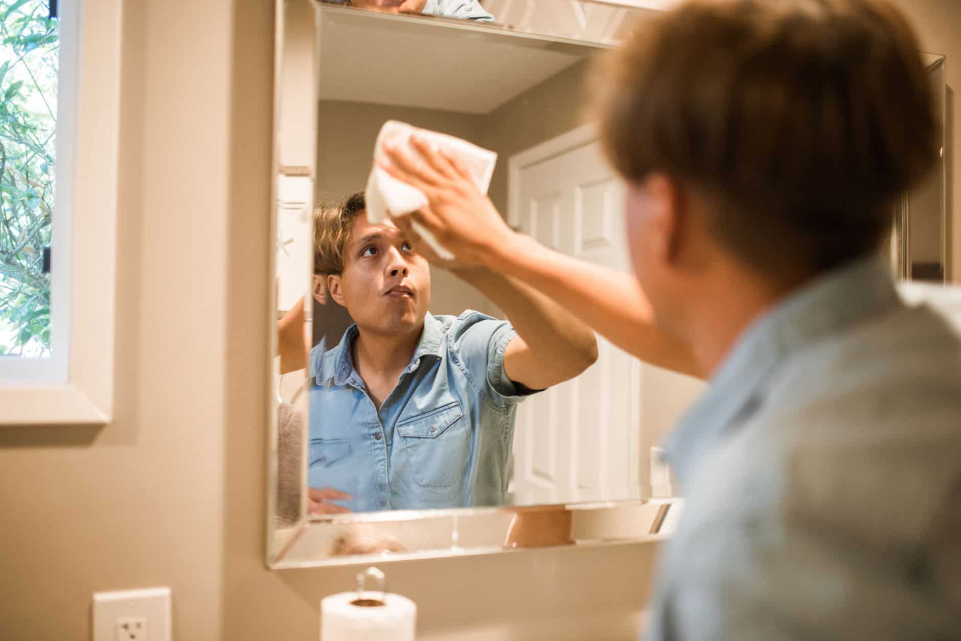 Man wiping a bathroom mirror with a white cloth