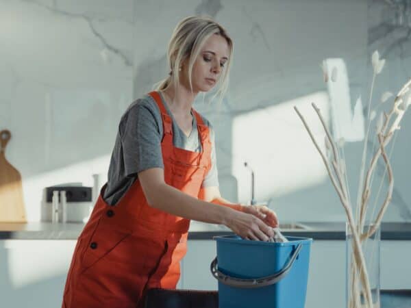 Woman in a kitchen wringing a cleaning cloth over a blue bucket