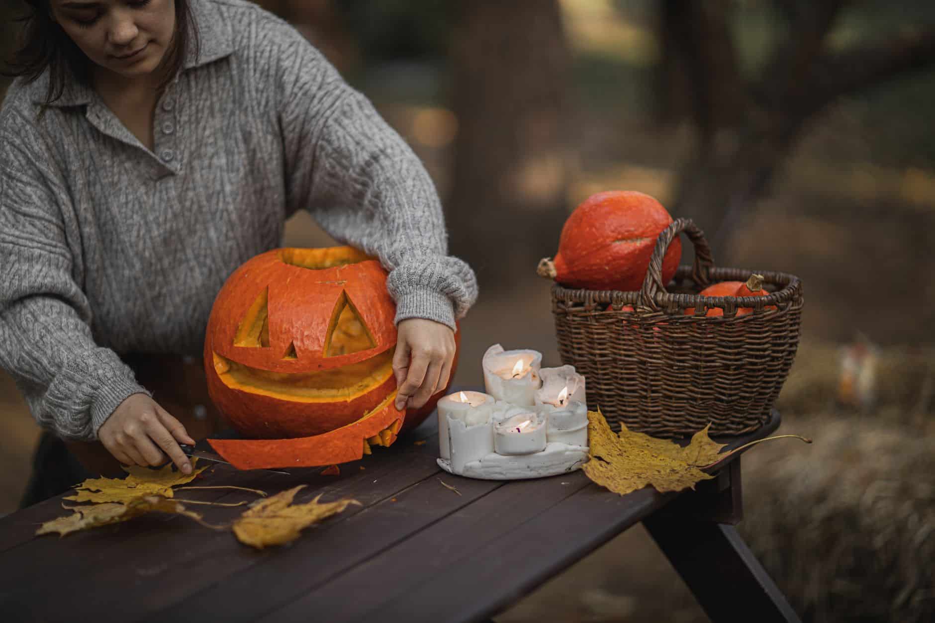 Woman carving a pumpkin with autumn leaves and candles