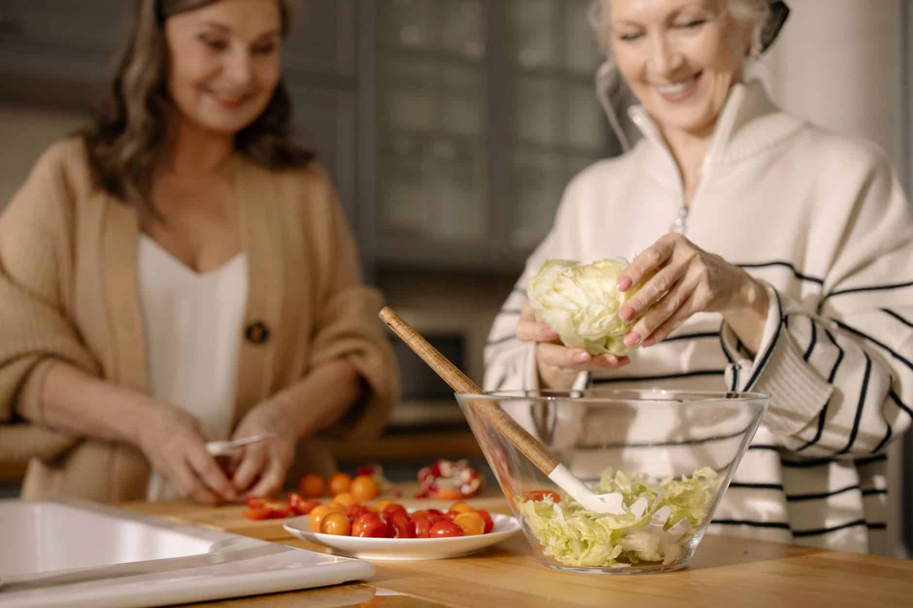 Two older women cooking together with tomatoes in the kitchen