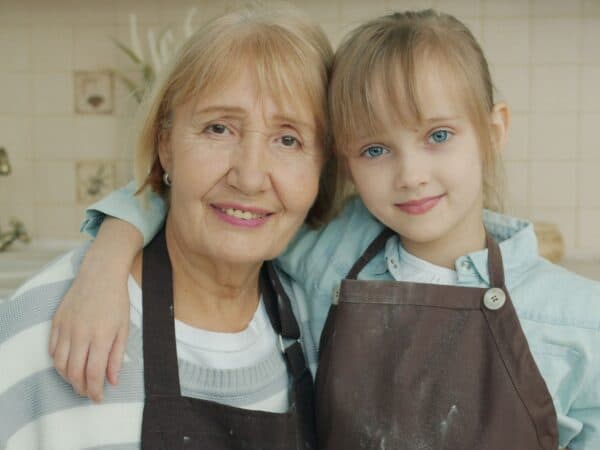 Grandmother and granddaughter in aprons smiling together in the kitchen