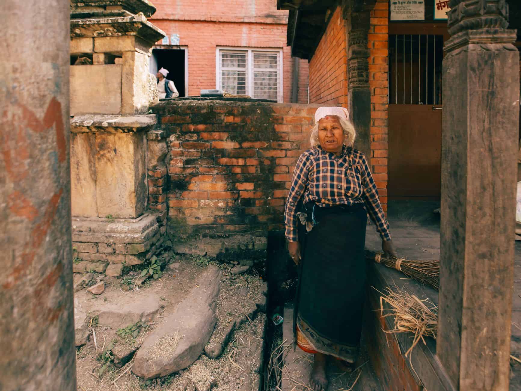 Grandmother standing with a broom outside her home