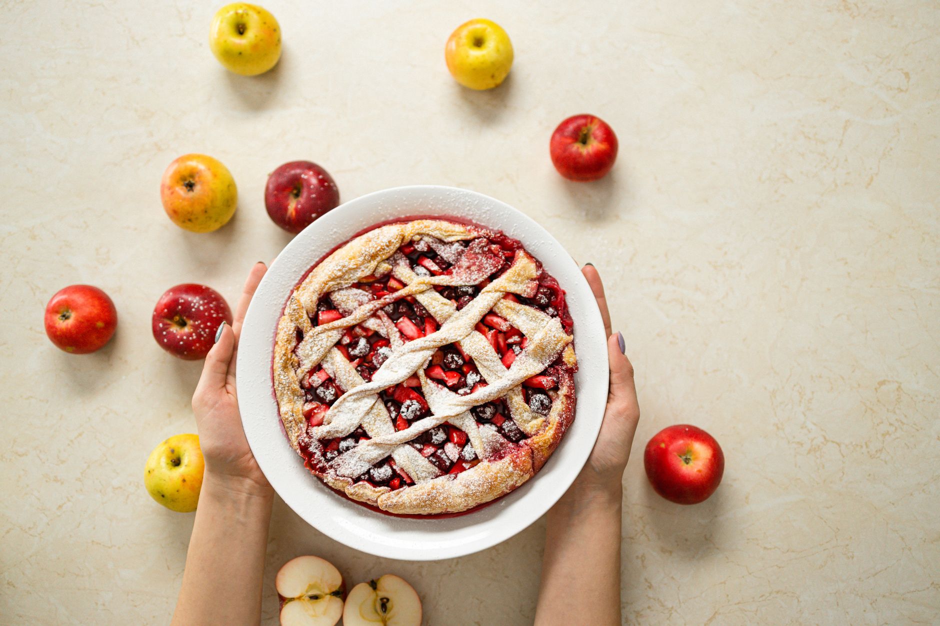Hands holding a freshly baked homemade pie surrounded by apples
