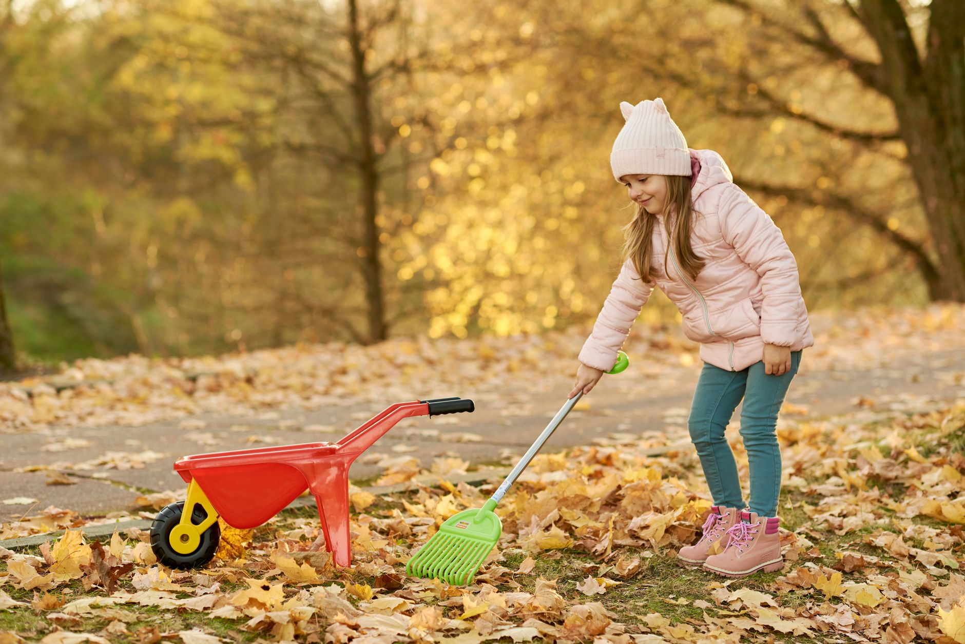 Young girl raking autumn leaves on a sunny fall day
