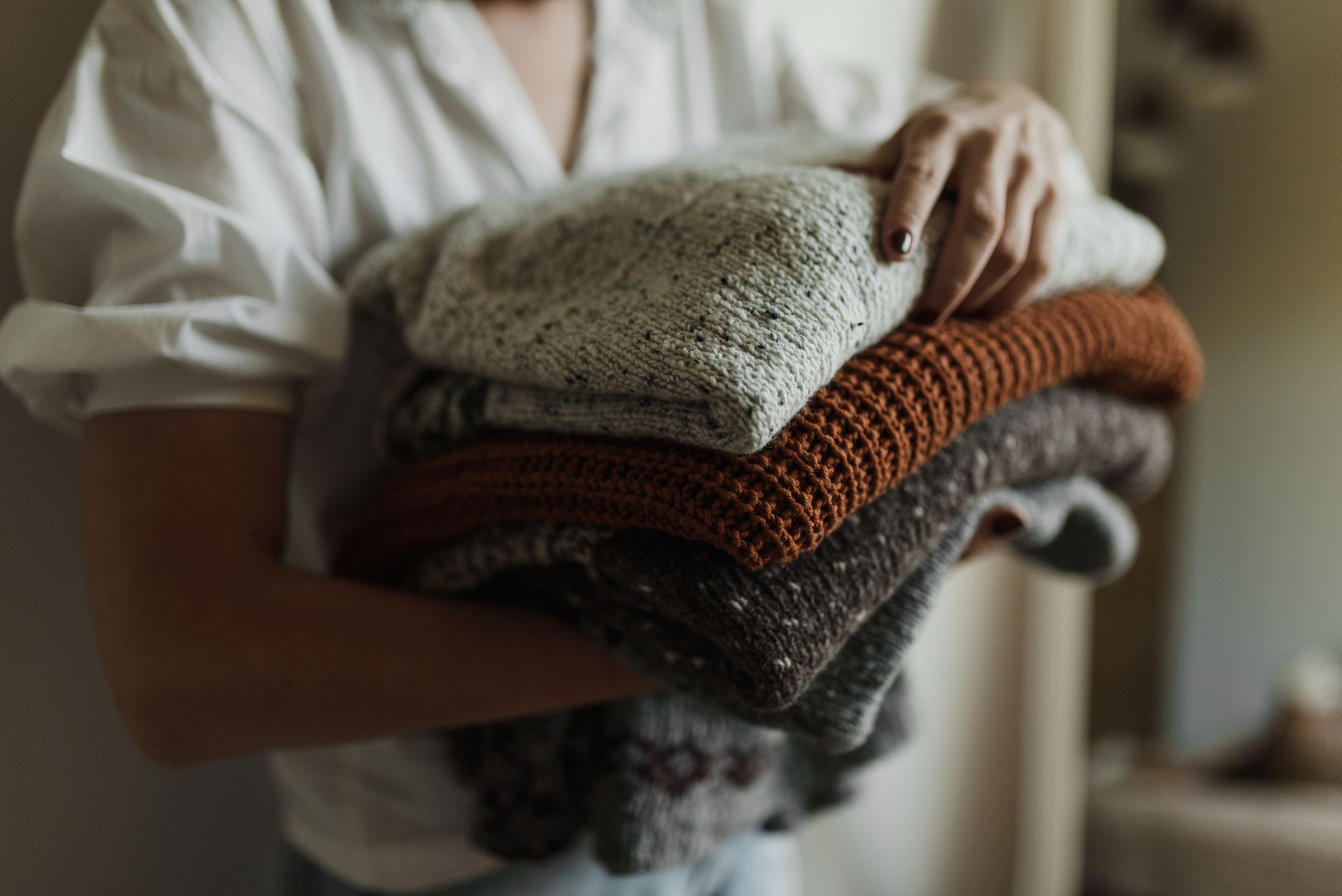 Woman holding a stack of folded knit sweaters in autumn colors